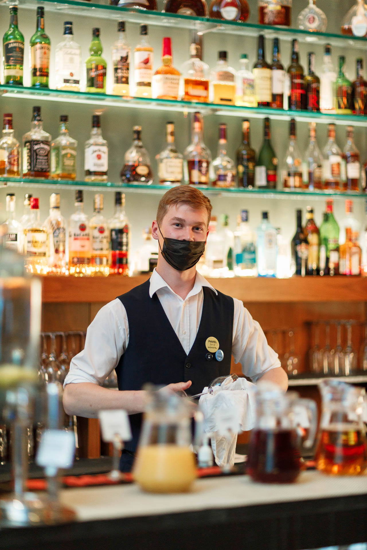 бармен в белой рубаке стоит за барной стойкой и натирает бокал перед банкетом