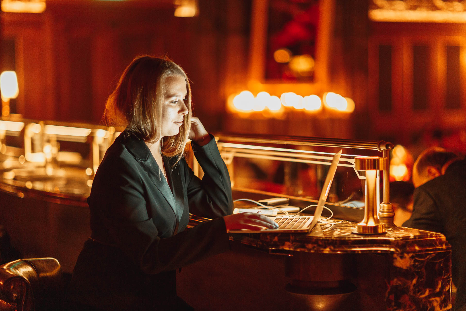 Сосредоточенная девушка, работающая за ноутбуком в тускло освещенном баре с теплым освещением