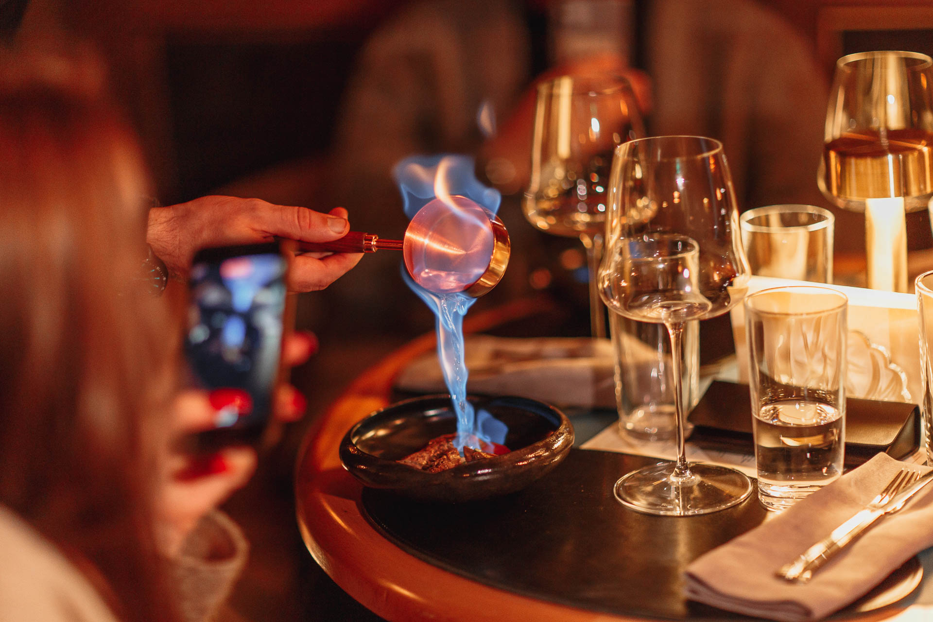 голубое пламя на кулинарном блюде в уютной обстановке с бокалами для вина и теплым рассеянным освещением
