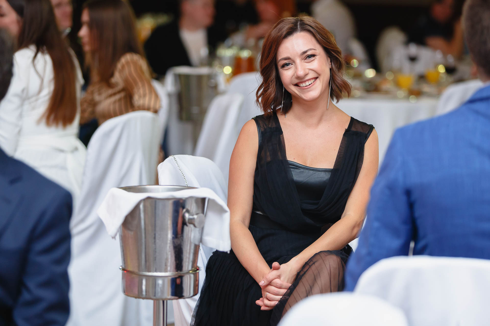 женщина улыбается фотографу на корпоративном мероприятии на фоне столов и гостей