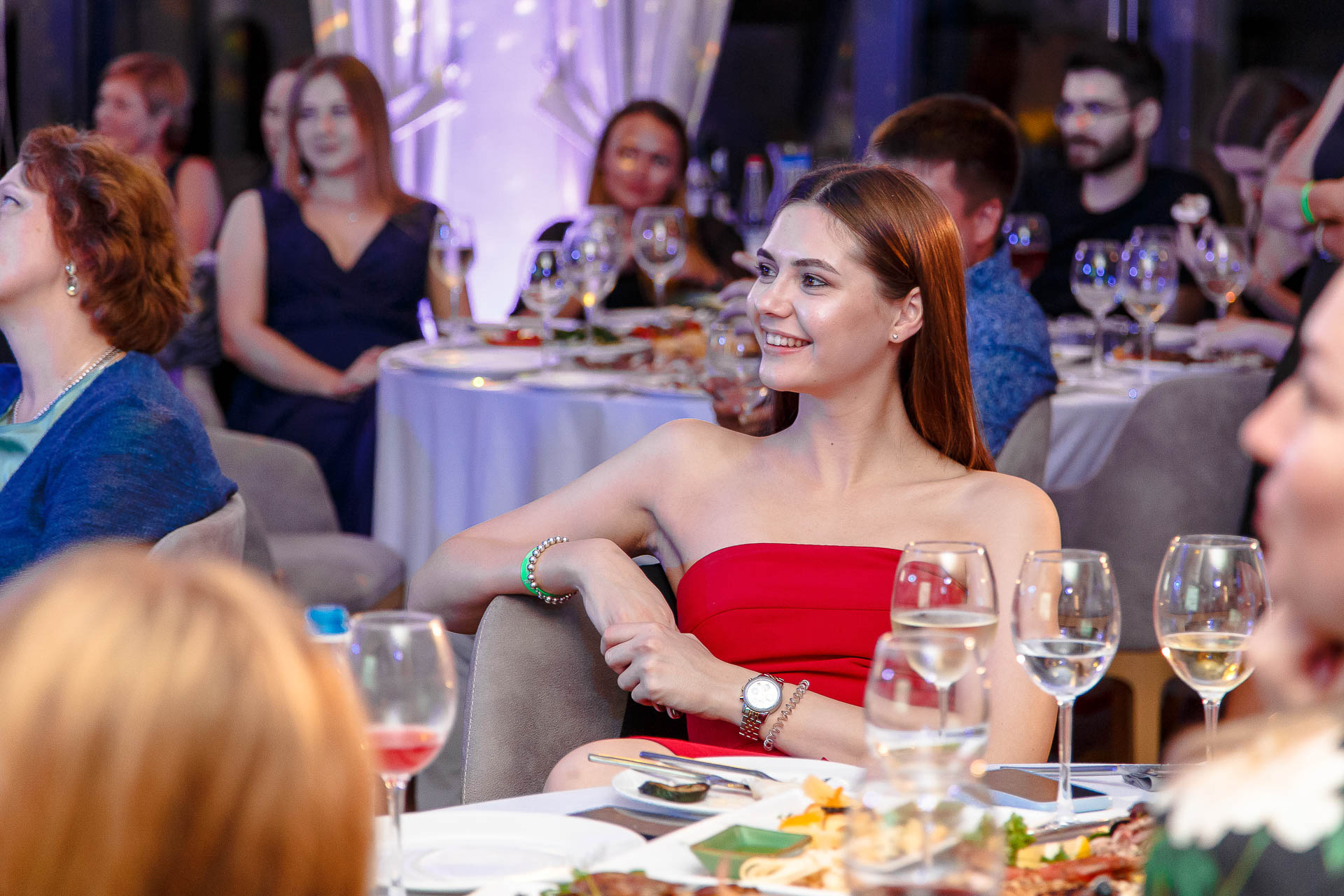 Улыбающаяся девушка в красном платье за столом на гала-ужине